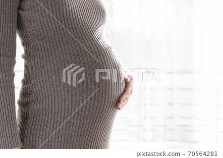Pretty young pregnant woman standing by the window in home Pretty young pregnant woman standing by the window in home 70564281