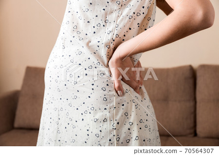 Pregnant woman hold back pain on sofa at thr home. Maternity healthcare concept support products 70564307