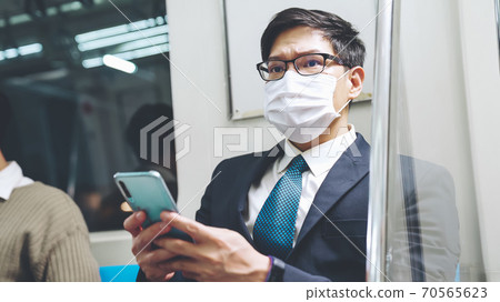 Traveler wearing face mask while using mobile phone on public train Traveler wearing face mask while using mobile phone on public train 70565623