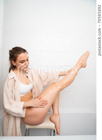 girl apply moisturizer cream on leg in bathroom. girl apply moisturizer cream on leg in bathroom. 70565892