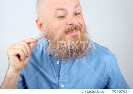 man in a blue denim shirt touches his beard 70567624