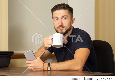 business man with cup and cell phone in hand sitting at the table business man with cup and cell phone in hand sitting at the table 70567632