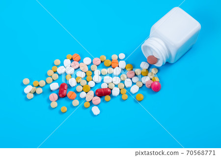 Medical pills and tablets spilling out of a drug bottle on blue background 70568771