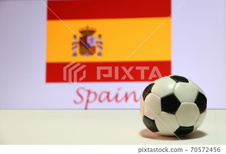 Small football on the white floor and Spanish nation flag with the text of Spain background. Small football on the white floor and Spanish nation flag with the text of Spain background. 70572456