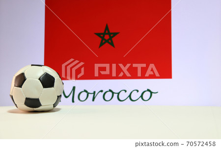 Small football on the white floor and Moroccan nation flag with the text of Morocco background. Small football on the white floor and Moroccan nation flag with the text of Morocco background. 70572458