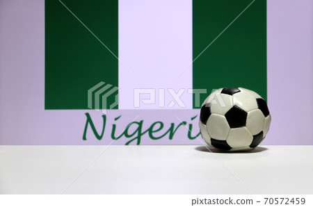 Small football on the white floor and Nigerian nation flag with the text of Nigeria background. Small football on the white floor and Nigerian nation flag with the text of Nigeria background. 70572459