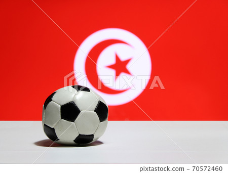 Small football on the white floor and Tunisian nation flag with moon and star background. Small football on the white floor and Tunisian nation flag with moon and star background. 70572460