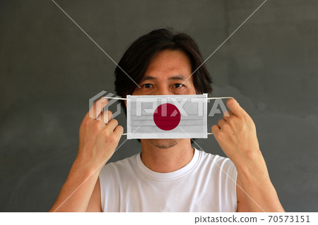 A man with Japan flag on hygienic mask in his hand and lifted up the front face A man with Japan flag on hygienic mask in his hand and lifted up the front face 70573151