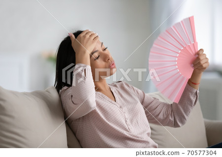 Overheated biracial woman use hand fan at home 70577304