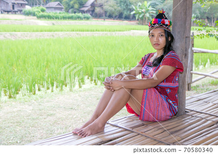 Asian woman in traditional costume for Karen resting beside green rice field 70580340
