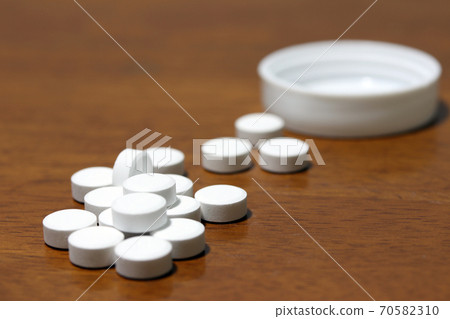 Pile of white round medicine on the wooden floor and white plastic cap. Pile of white round medicine on the wooden floor and white plastic cap. 70582310
