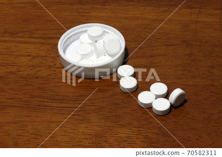 Pile of white round medicine on the wooden floor and white plastic cap. 70582311