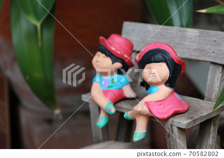 colorful clay doll boy and girl sitting on small wooden chesterfield. 70582802