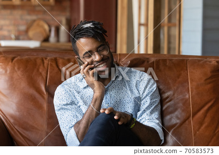 Smiling African American man talk on smartphone at home Smiling African American man talk on smartphone at home 70583573