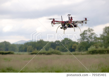 Hex copter camera drone hovers in front of a rural background. Hex copter camera drone hovers in front of a rural background. 70585401