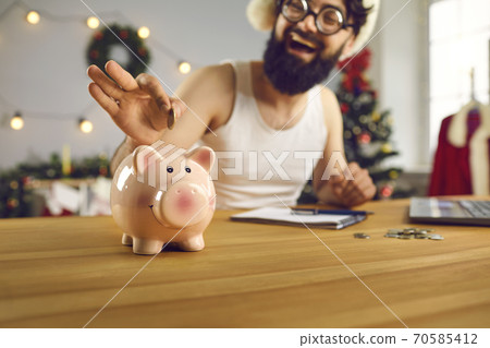Happy young man decides to start saving up in the new year and puts money in smiley piggy bank 70585412