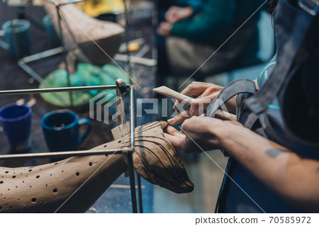 Close-up view of female hands gently handling a clay whale in workshop. Close-up view of female hands gently handling a clay whale in workshop. 70585972