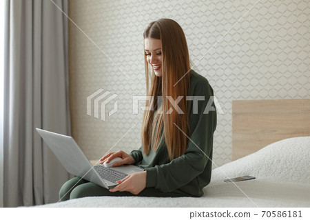 Woman sitting on a bed and uses a laptop Woman sitting on a bed and uses a laptop 70586181