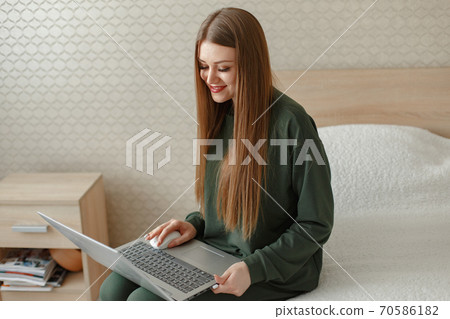 Woman sitting on a bed and uses a laptop Woman sitting on a bed and uses a laptop 70586182