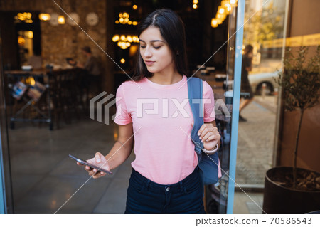 Caucasian attractive young woman walking out the door of a cafe. 70586543