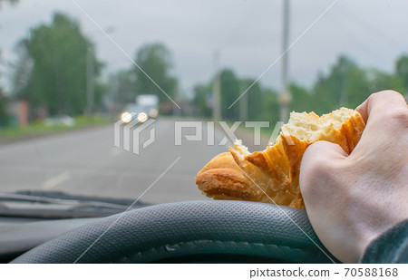 a bitten bun in the hand of a driver at the wheel of a car 70588168