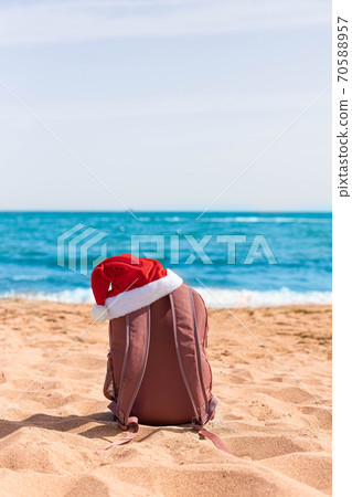 Santa hat on a sports backpack lying on the beach of the sea coast. Christmas beach holiday travel poster 70588957