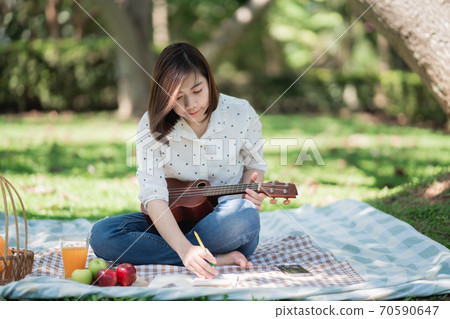 asian women sitting on the grass during a picnic and writing song in a park 70590647