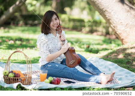 asian women sitting on the grass during a picnic and writing song in a park 70590652