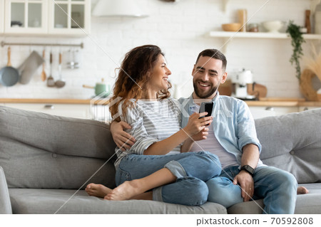 Happy young couple using smartphone together, relaxing on couch 70592808