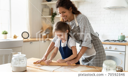 Smiling loving mother and little daughter rolling out dough together Smiling loving mother and little daughter rolling out dough together 70592846