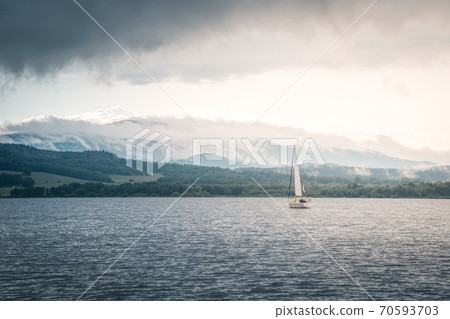 Sailing boat floats on the lake with stormy clouds sky. Autumn sailboat ship water sport scene from Lipno, Czech republic, Sumava. 70593703