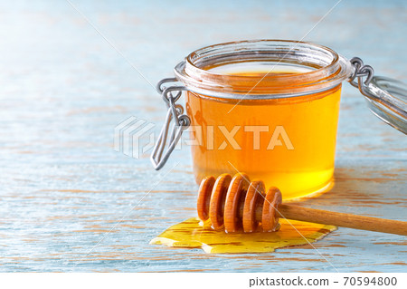 open jar of honey on a blue table, selective focus. open jar of honey on a blue table, selective focus. 70594800