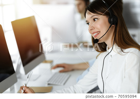 Asian woman working at customer service office. Business concept. Group of diverse operators at work in sunny call center. 70595094