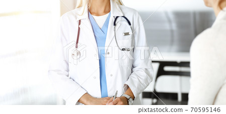 Unknown woman-doctor communicating with female patient in sunny clinic. Physician checks medical history record and exam results, close-up Unknown woman-doctor communicating with female patient in sunny clinic. Physician checks medical history record and exam results, close-up 70595146