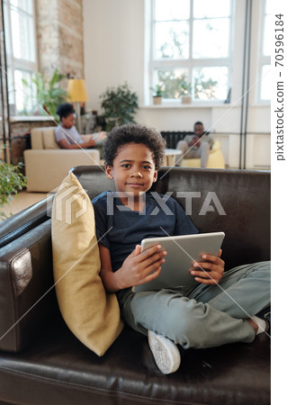 Adorable little boy in casualwear sitting on couch and watching online video 70596184