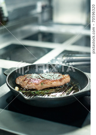 Hot roasted beef steak seasoned with fresh aromatic herbs on grill frying pan Hot roasted beef steak seasoned with fresh aromatic herbs on grill frying pan 70596320