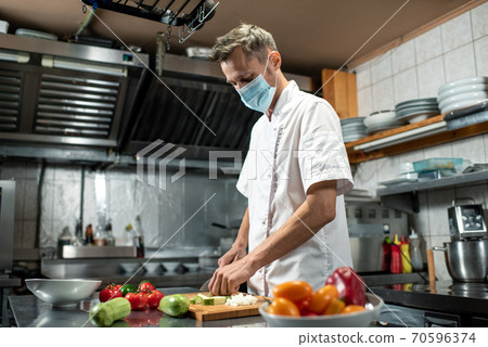 Professional young chef in uniform and protective mask chopping fresh zucchini 70596374