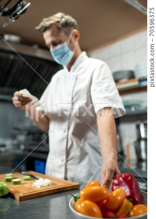 Contemporary young chef in uniform and protective mask taking bowl with capsicum 70596375