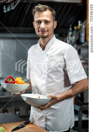 Young chef holding two ceramic bowls with fresh capsicum for vegetable course Young chef holding two ceramic bowls with fresh capsicum for vegetable course 70596389