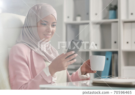 Happy restful Muslim businesswoman in hijab scrolling in smartphone at break 70596465