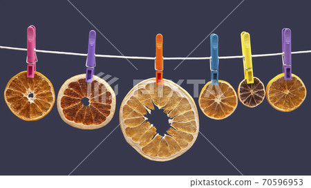 dried pieces of different citrus fruits hang on colored clothespins on a blue background 70596953