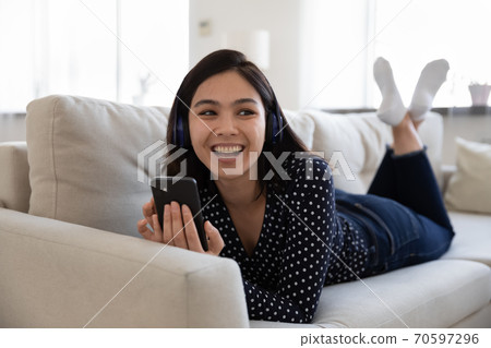 Excited Asian girl in headphones use smartphone 70597296
