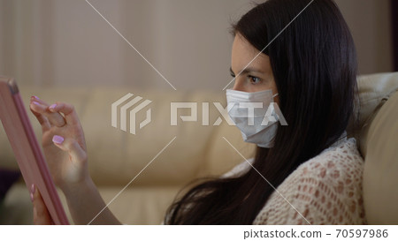 Woman in a Medical Mask Uses a Tablet at Home During Quarantine. Works Alone From Home Remotely. Quarantine Covid-19 Corona Virus. Social Distancing Concept. 70597986