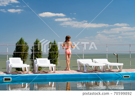 girl in bathing suit between sun loungers by pool 70599892