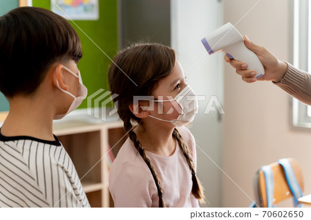 Group of Caucasian students in school building checked and scanned for temperature check. Elementary pupils are wearing a face mask and line up before entering into classroom. Group of Caucasian students in school building checked and scanned for temperature check. Elementary pupils are wearing a face mask and line up before entering into classroom. 70602650