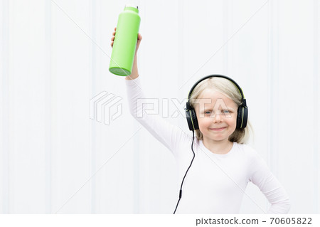 Young blond girl on white background drink fresh spring water from green reusable bottle. Healthy lifestyle in summer city. Young blond girl on white background drink fresh spring water from green reusable bottle. Healthy lifestyle in summer city. 70605822