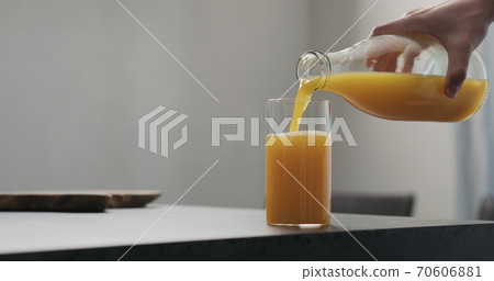 man pour orange juice from glass bottle into highball glass on concrete countertop with copy space 70606881