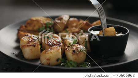 eat roasted scallops with baked potatoes on black plate 70606968