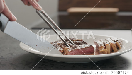 Man slicing ribeye steak on a white plate on concrete countertop Man slicing ribeye steak on a white plate on concrete countertop 70607174