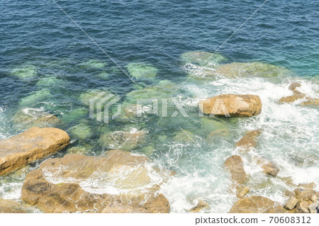 Surf with foamy waves on a sunny calm day and rocky shore Surf with foamy waves on a sunny calm day and rocky shore 70608312